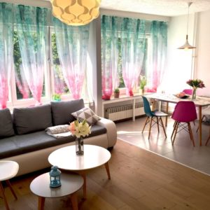 Airbnb Living Room with Couch, Round Table with Flowers, Big Windows with Curtains, Dining Table with Chairs
